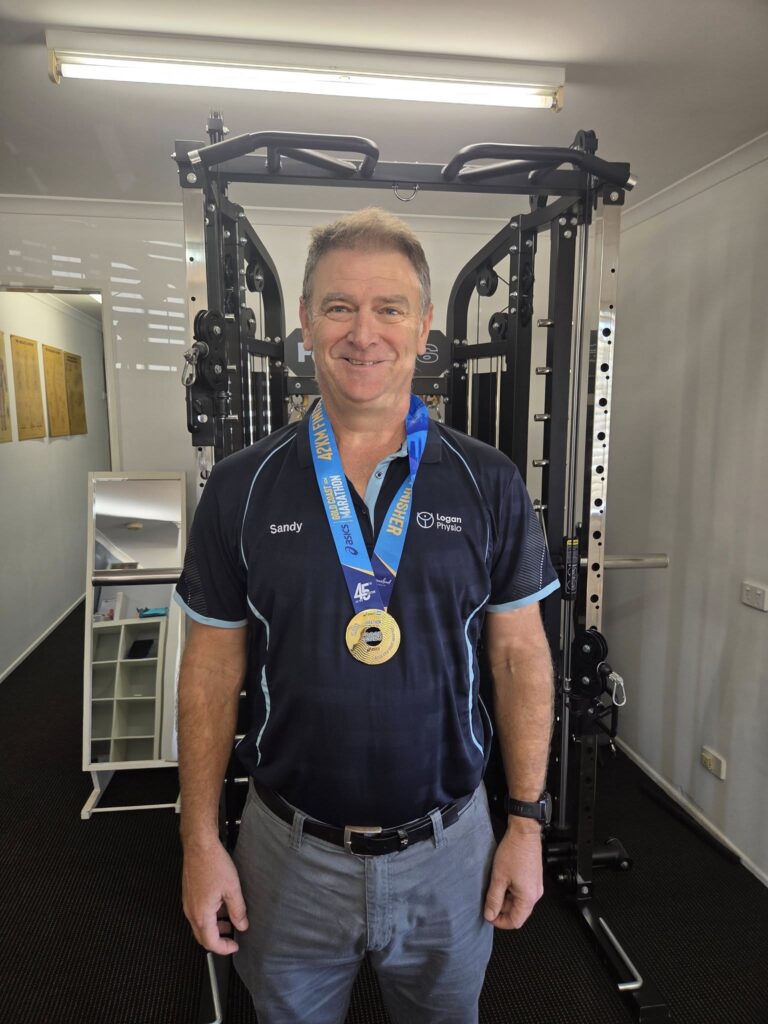 Sandy in the clinic wearing his Gold Coast Marathon 2025 medal